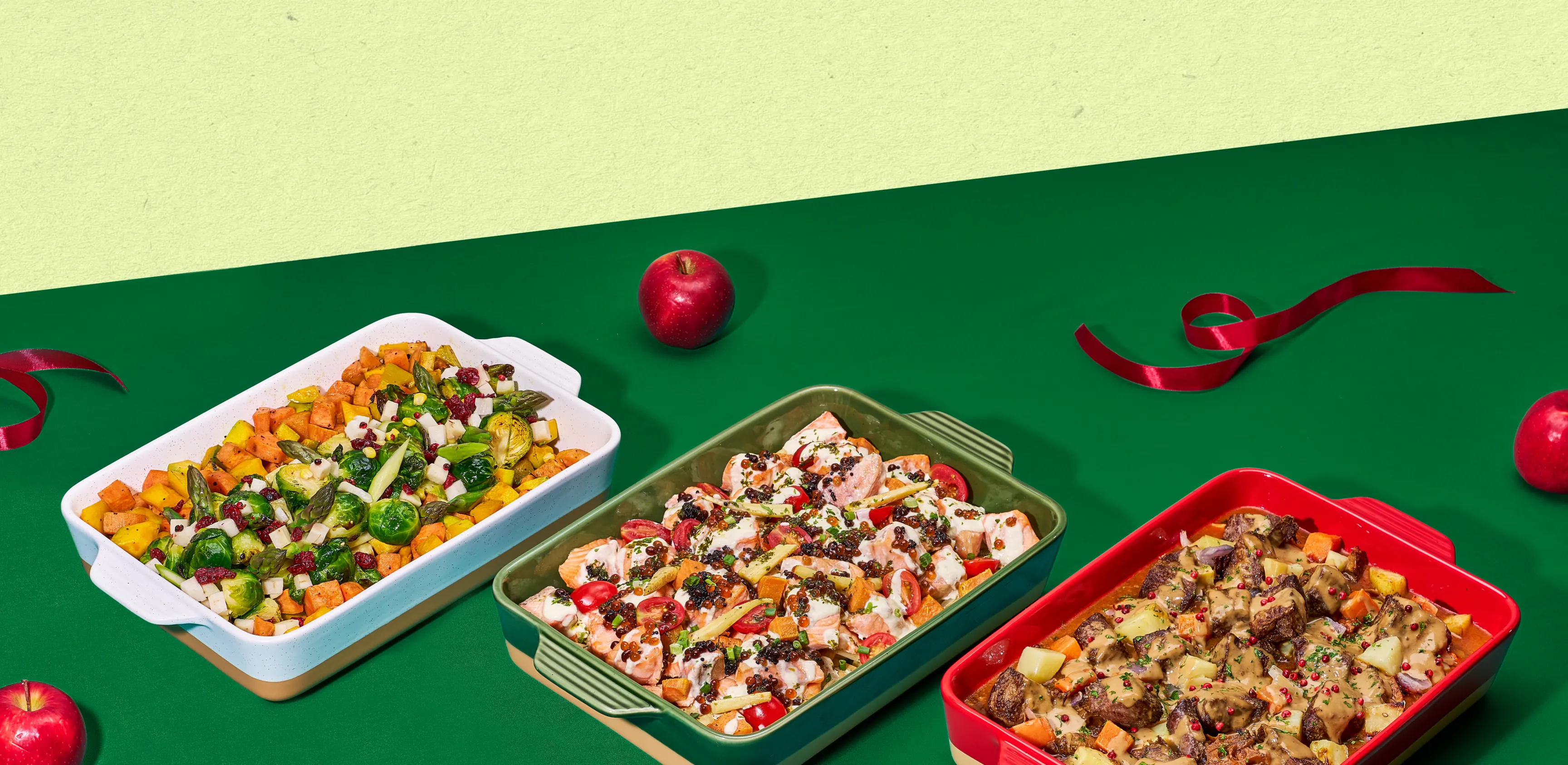Christmas dishes in serving trays on a green table with apples and ribbon